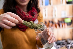 a woman putting a large bud of weed into a jar at a weed dispensary