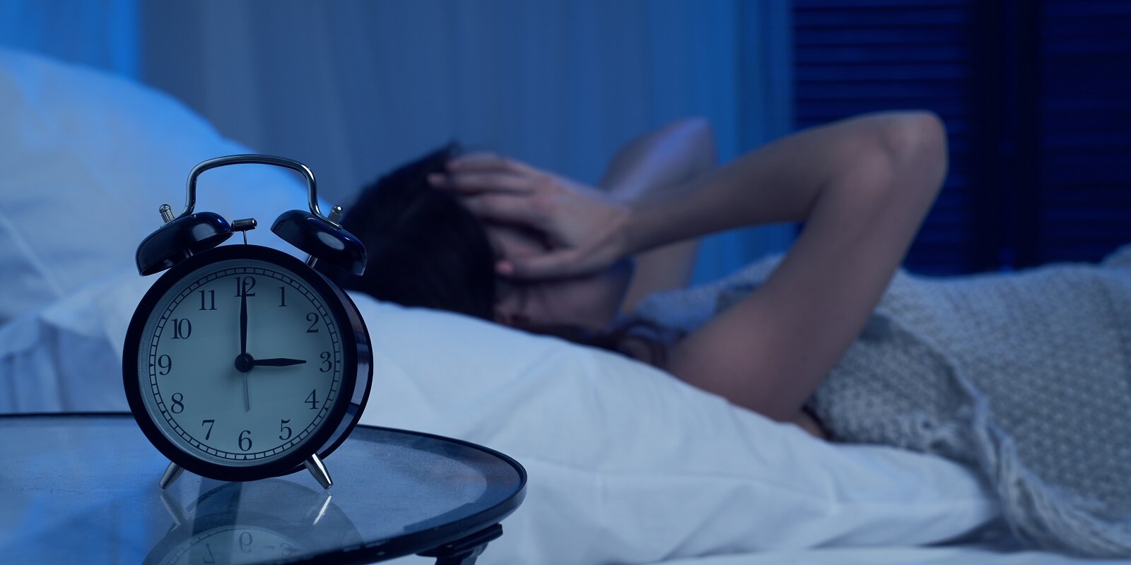 unhappy woman with insomnia lying on bed next to alarm clock at night