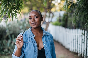 Black woman hold up cannabis concentrate vape pen outside