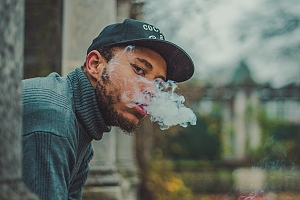 Bearded mixed male wearing green turtleneck blows out cannabis flower smoke