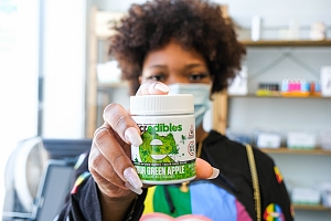 Cannabis dispensary worker wearing mask holding weed edible product