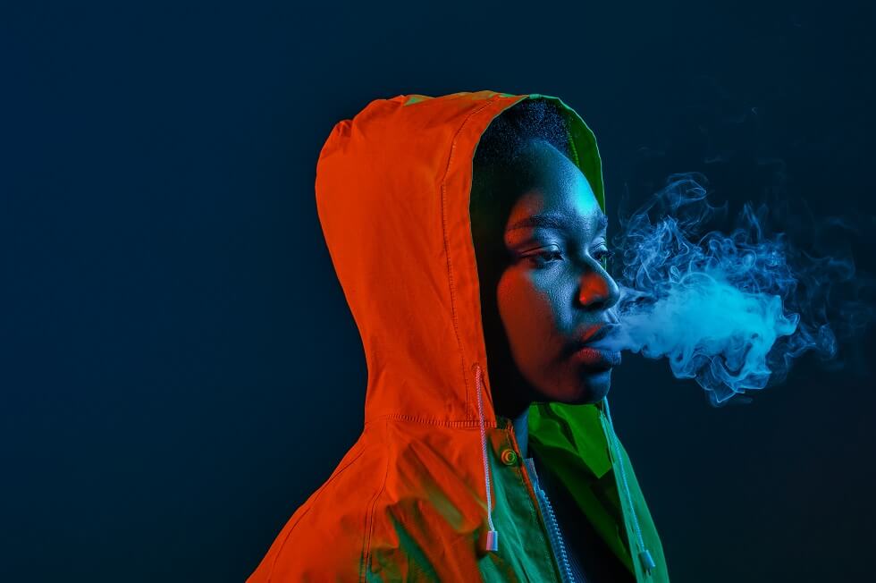 African American woman in yellow raincoat blowing smoke from mouth