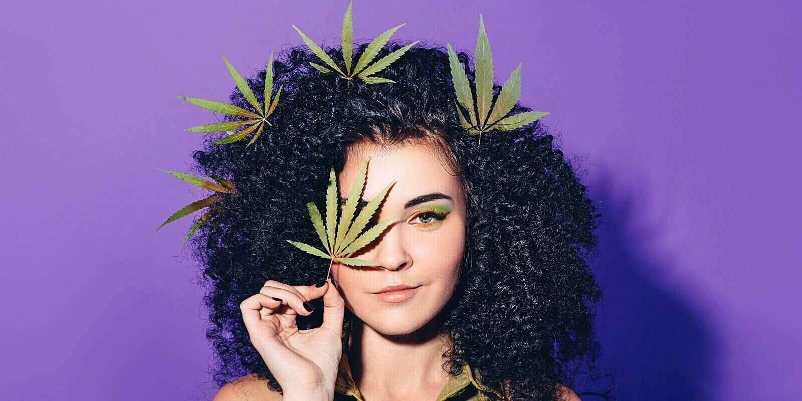 mixed race woman with afro curls holding hemp leaf