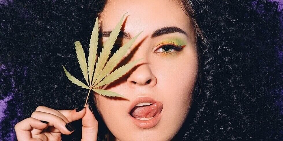 rastafarian woman with cannabis leaf near face
