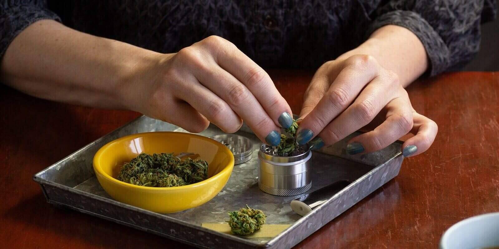 putting marijuana buds or hemp flowers in metal grinder in tray with smoking accessories