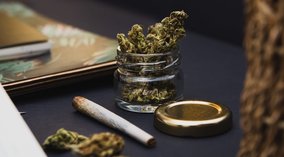 cannabis buds, gold lid, notebooks, joint on black background