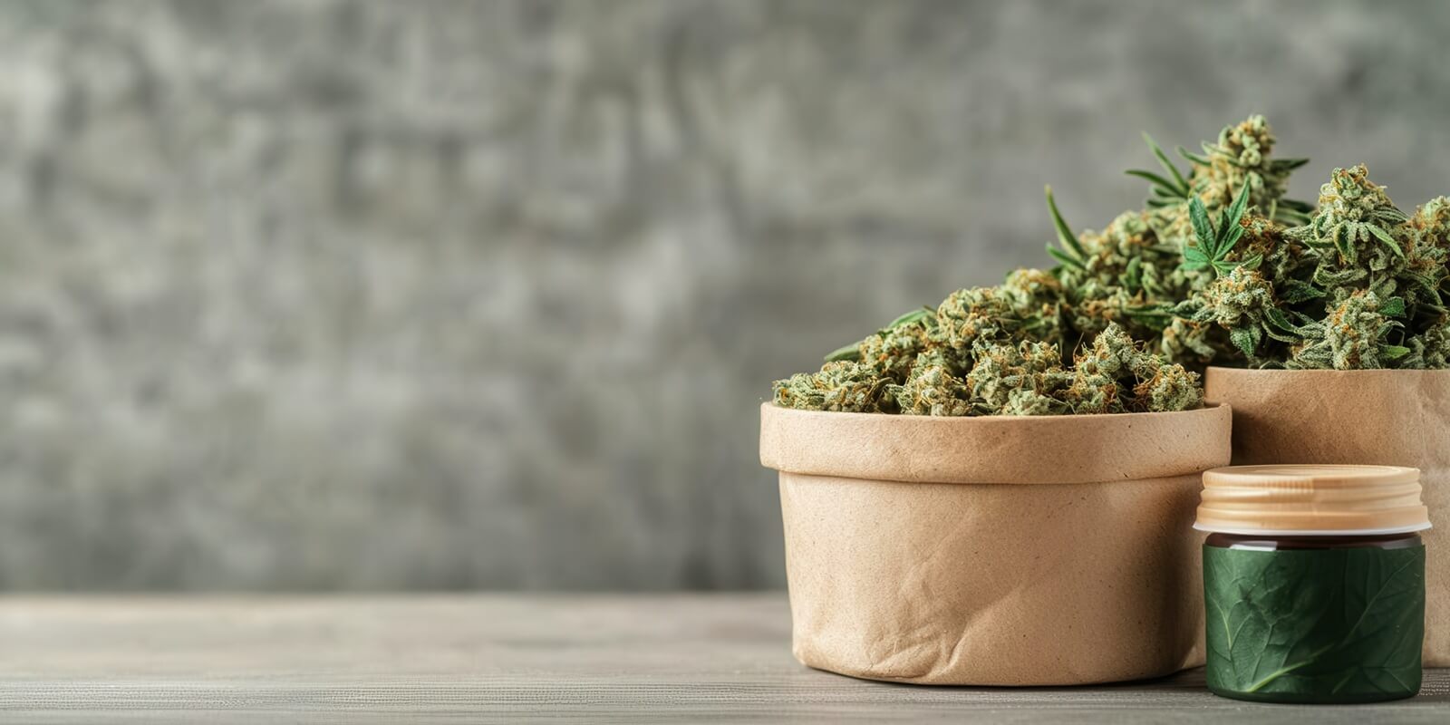 close-up of potted cannabis plants and a small jar for edibles on a wooden table with a textured gray background